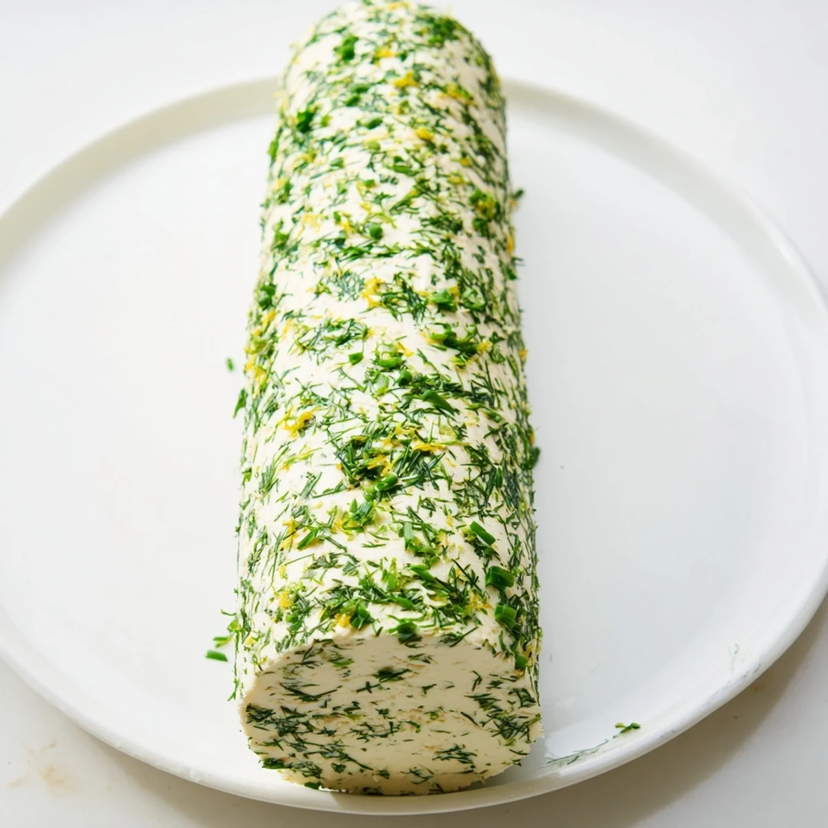 Close-up of a herby, creamy herb-coated cheese log with a ring of colorful, crunchy crackers for dipping.