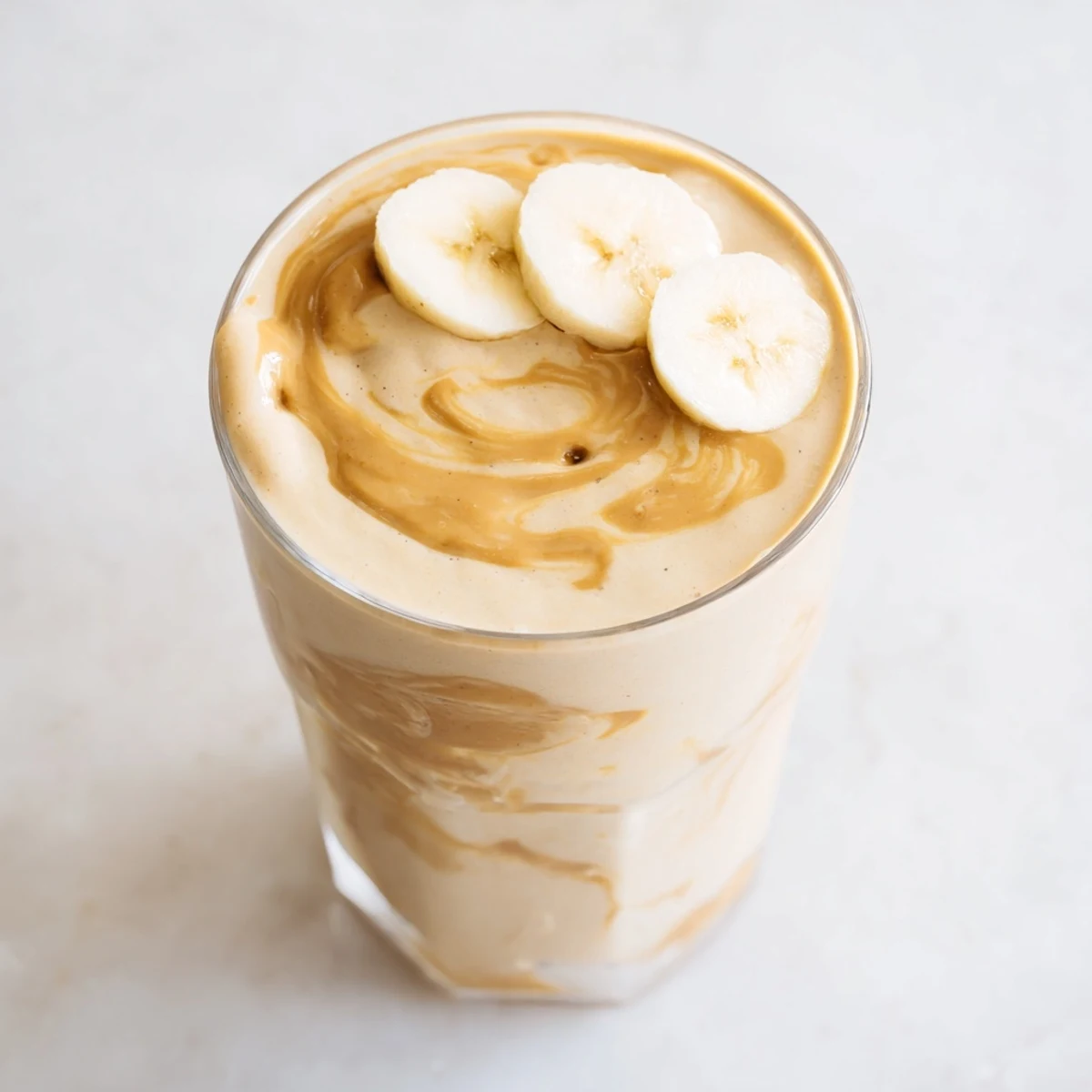 Freshly blended peanut butter banana smoothie, swirled with vanilla, served cold in a glass.