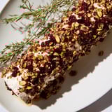 A close-up of a festive Cranberry Goat Cheese Logs board, showcasing colorful grapes, crackers, and honey drizzle.