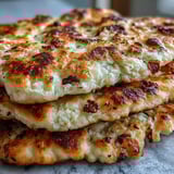 Two warm pieces of The Best Easy Garlic Naan Bread resting beside a rich curry bowl.