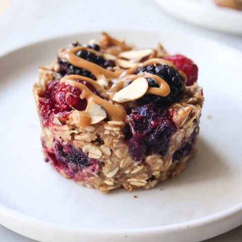 Warm, golden baked oatmeal cups with winter berries and a drizzle of almond butter, ready to eat.
