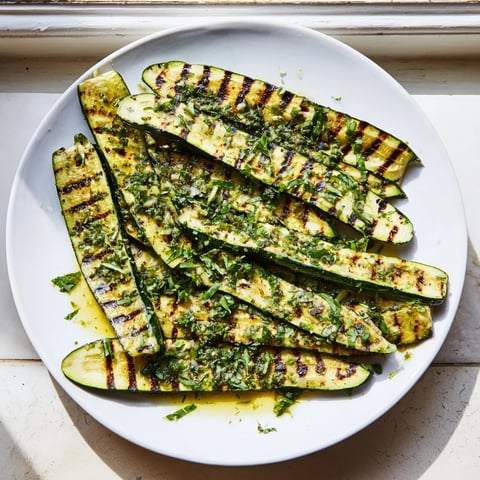 Grilled zucchini glistening with marinade, showing grill marks; a Mediterranean Garlic Herb Grilled Zucchini side.