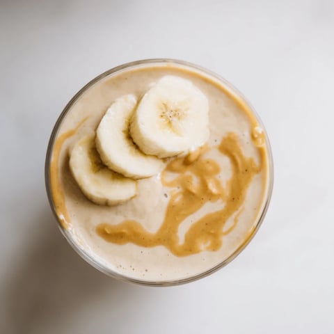 A tall glass overflowing with a creamy peanut butter banana smoothie, perfect for breakfast.