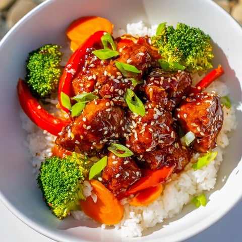Golden-brown teriyaki chicken glistening atop fluffy rice, served with colorful steamed vegetables, ready to eat.