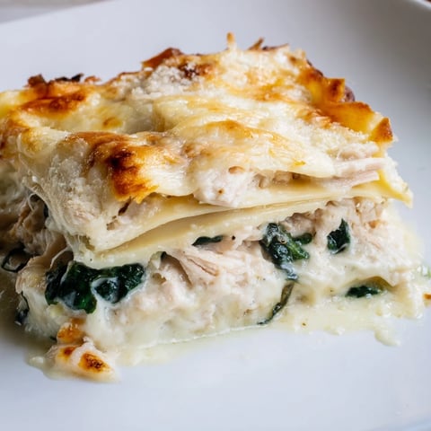Golden-brown Chicken Alfredo Lasagna bubbling from the oven, featuring creamy layers of shredded chicken, spinach, and melted mozzarella.