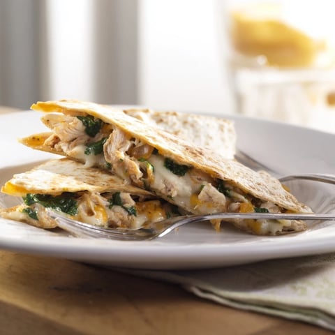A golden-brown Chicken and Spinach Quesadilla sliced into wedges, revealing layers of melted mozzarella and sautéed spinach.  