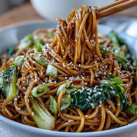 Asian Ginger Scallion Noodles with Sautéed Greens in a glossy bowl, garnished with sesame seeds and fresh chili slices.  