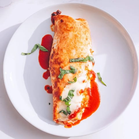 A handheld Crispy Chicken Parm Wrap, featuring golden fried chicken, rich tomato sauce, and gooey cheese nestled in a soft burrito-sized tortilla.  