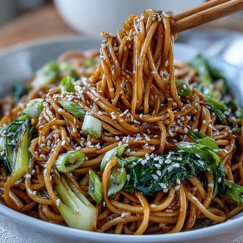 Asian Ginger Scallion Noodles with Sautéed Greens in a glossy bowl, garnished with sesame seeds and fresh chili slices.  