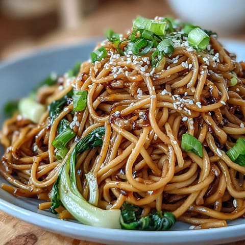 Vibrant ginger-scallion noodles tossed with tender bok choy and snap peas, served hot and aromatic in a ceramic dish.  